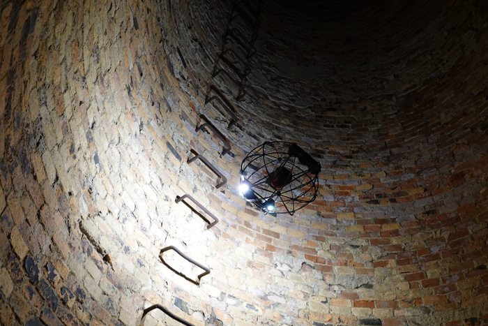 ASIO X drone flying with lights on inside a brick chimney with metal handlebars.